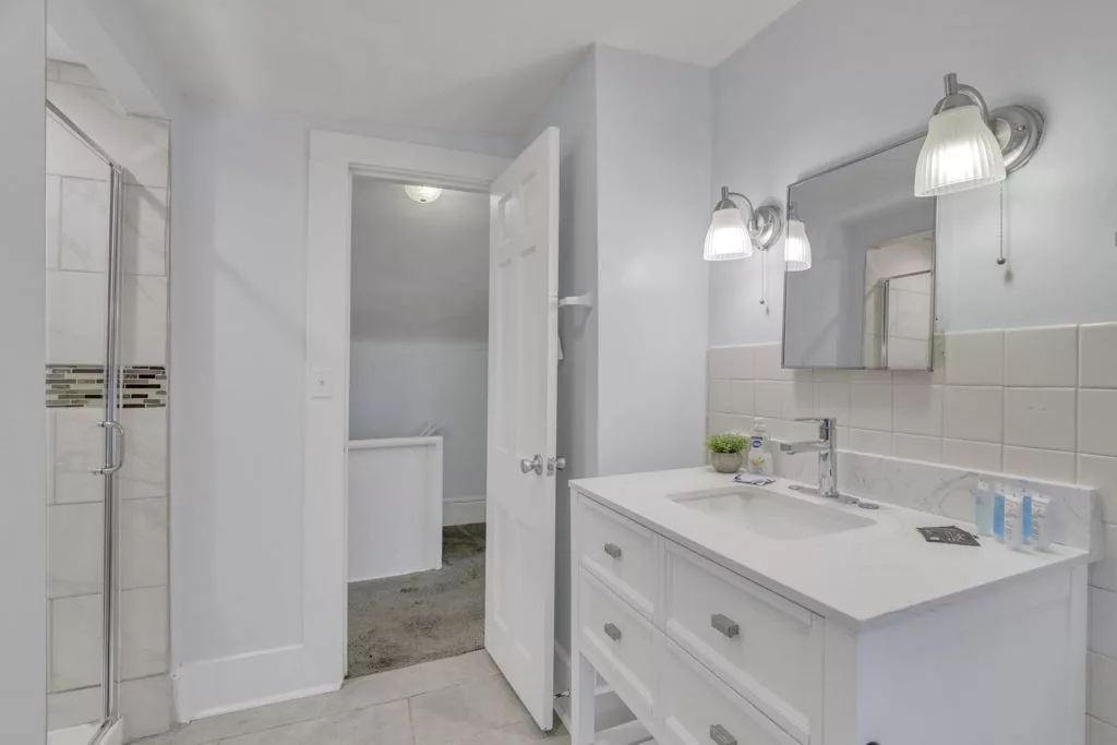 The Lantern bathroom with a white vanity, mirrored cabinet, wall lights, and a glass shower enclosure.
