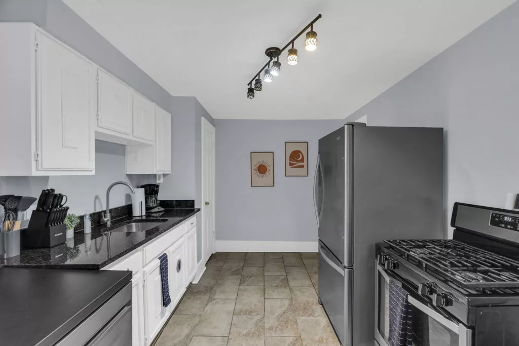The Lantern kitchen with white cabinets, dark countertops, a stainless steel refrigerator, and a gas range.