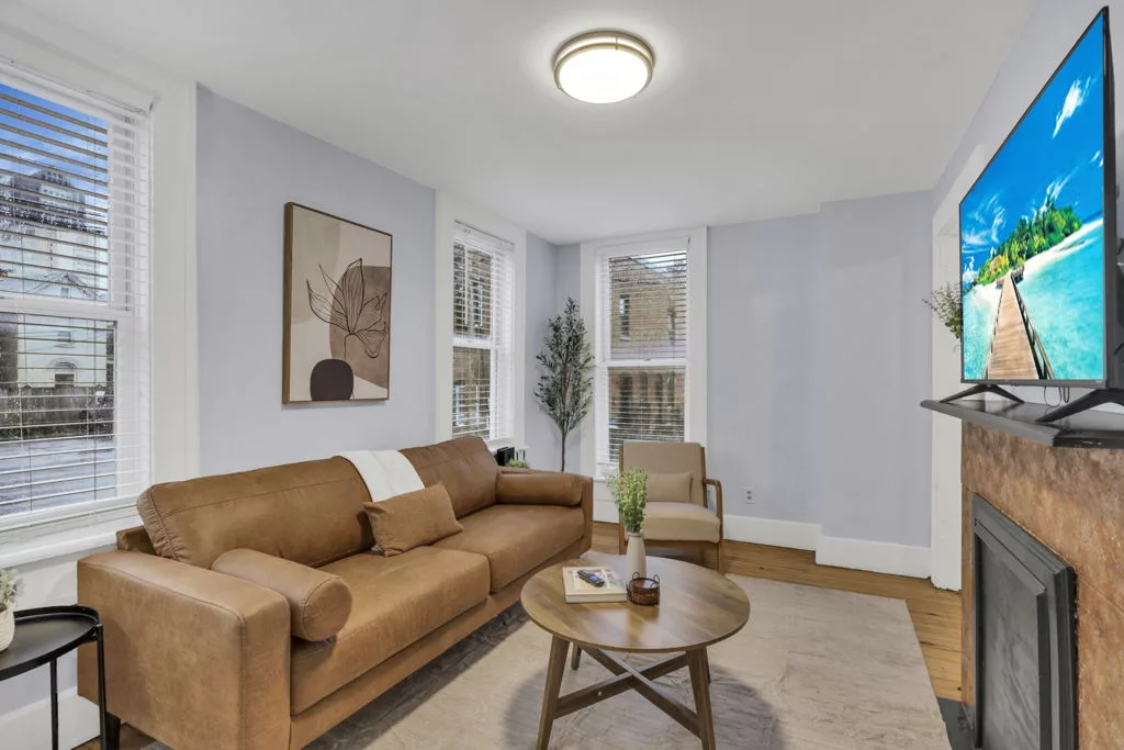 The Lantern living room with a caramel sofa, round coffee table, armchair, and tall windows.