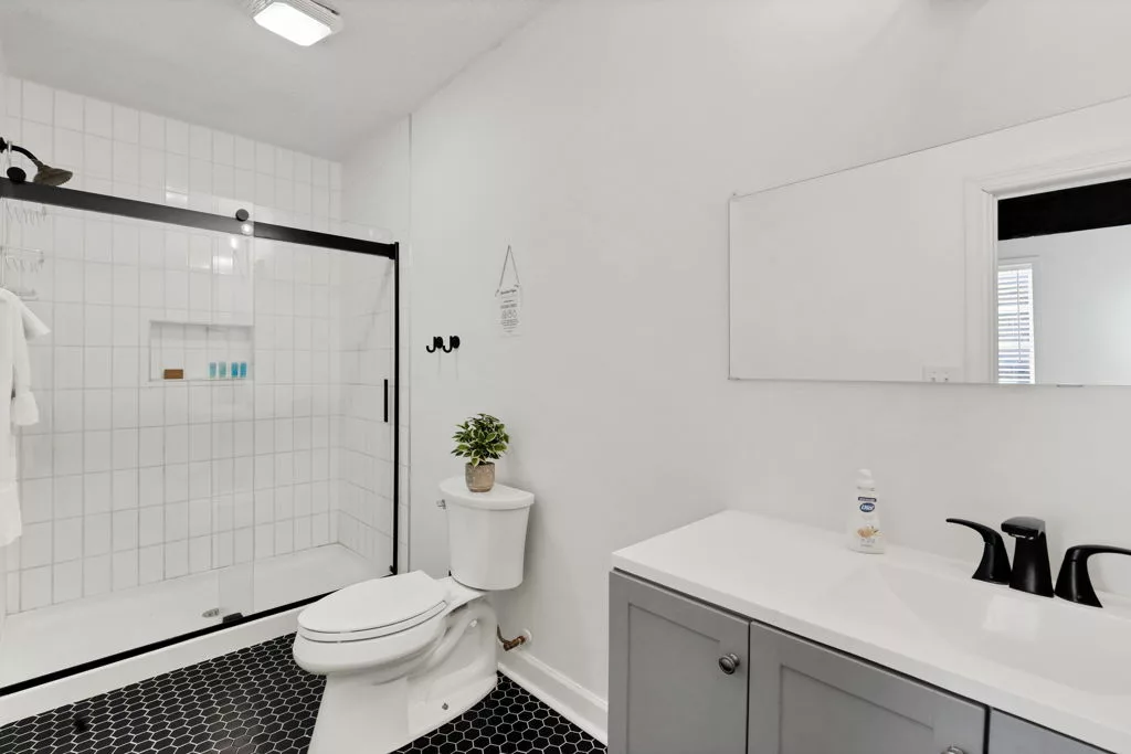 Bathroom with a gray vanity, white countertop, black fixtures, glass walk-in shower, and black hexagonal floor tile.