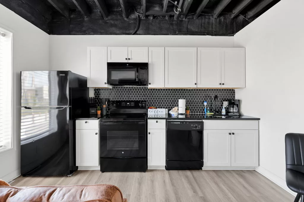 Full kitchen with white cabinets, black hexagonal tile backsplash, refrigerator, range, microwave, and dishwasher.