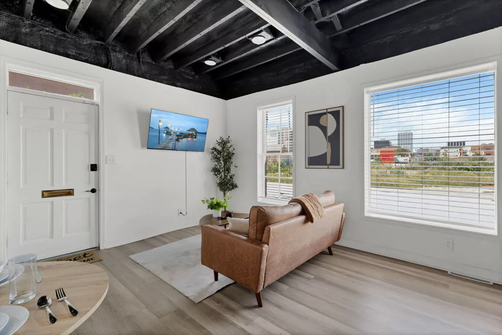 Orange sofa facing a wall-mounted television in a living room with tall windows and exposed black ceiling beams.