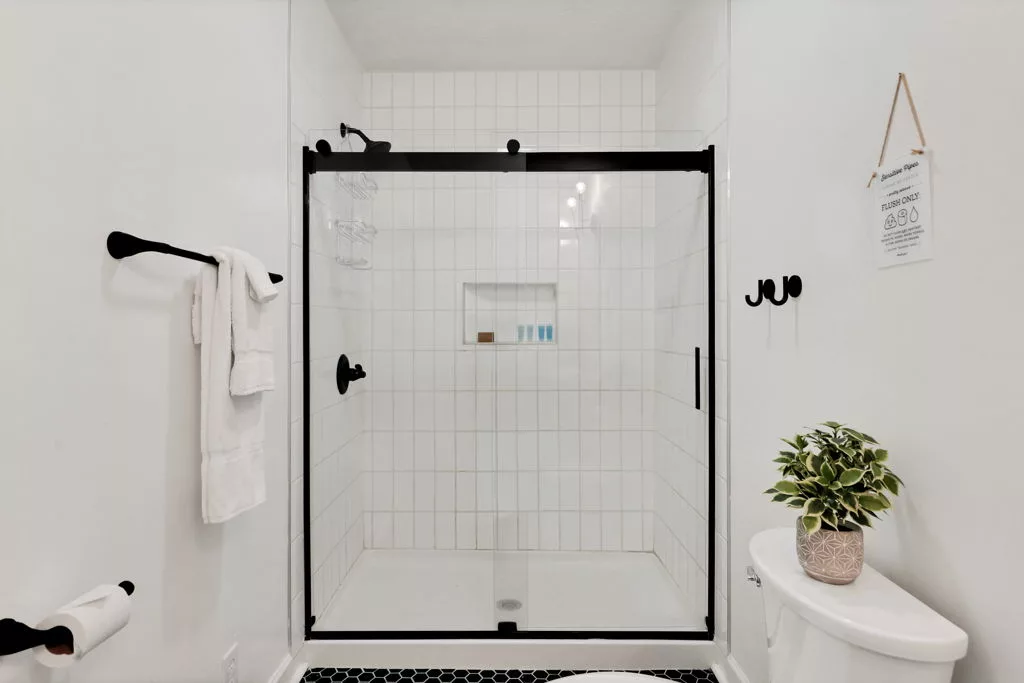 Glass walk-in shower with white tile, black fixtures and door frame, and an inset shelf.